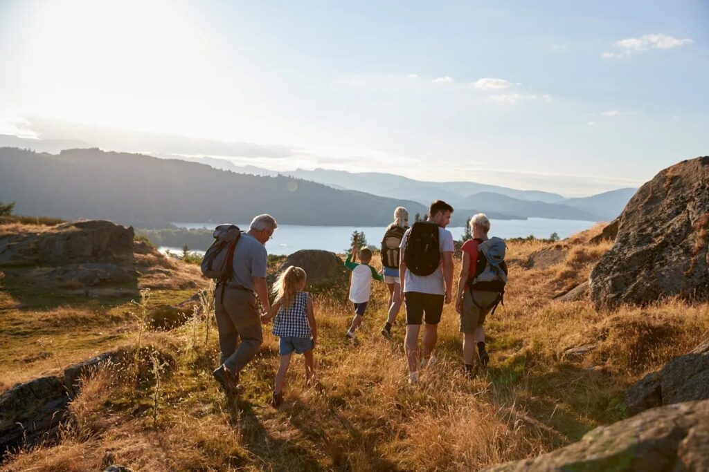 Family hiking together on a sunny hillside overlooking a lake.